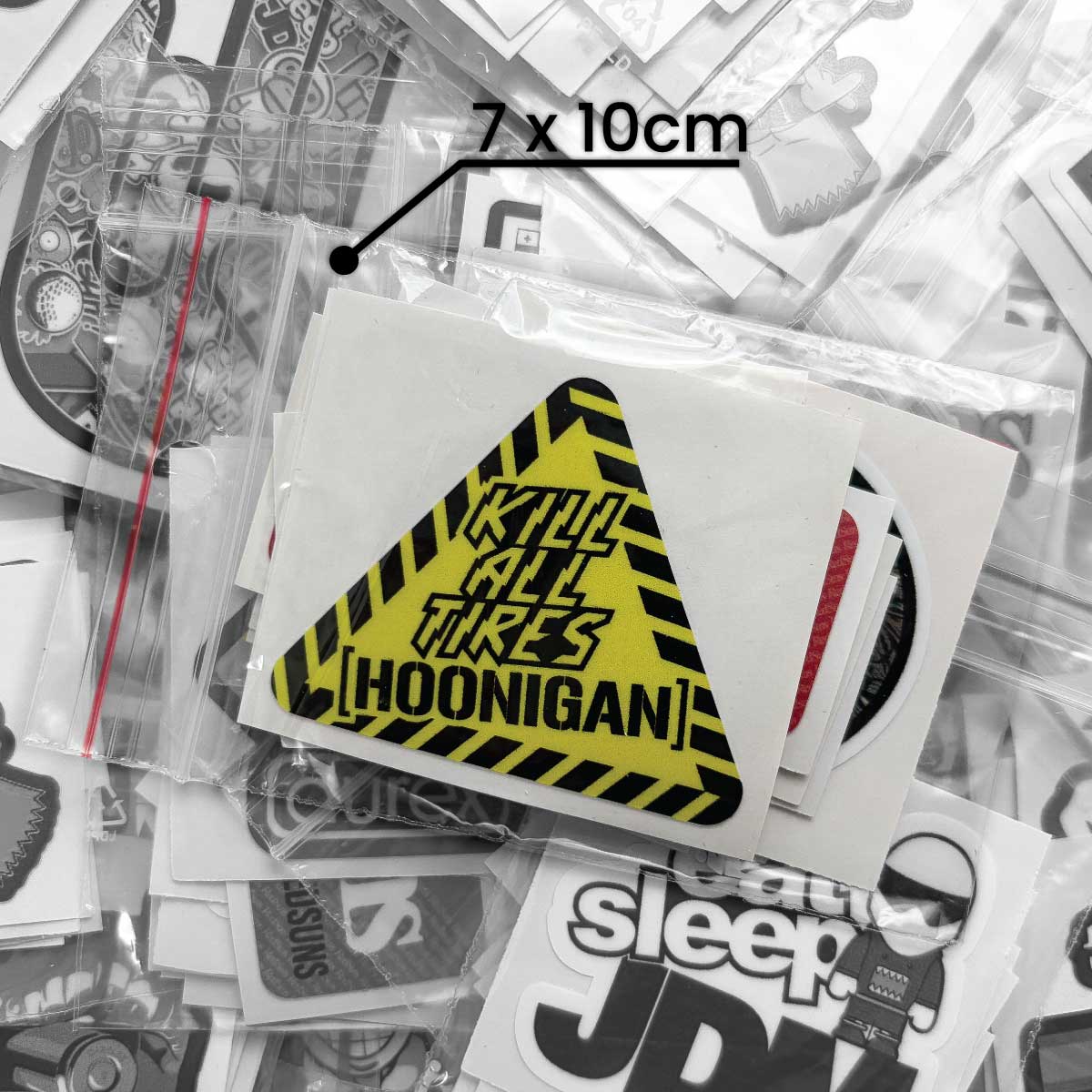 Žltá nálepka Hoonigan s čierno-žltým výstražným vzorom má rozmer 7 × 10 cm a leží medzi ďalšími nálepkami v balení.